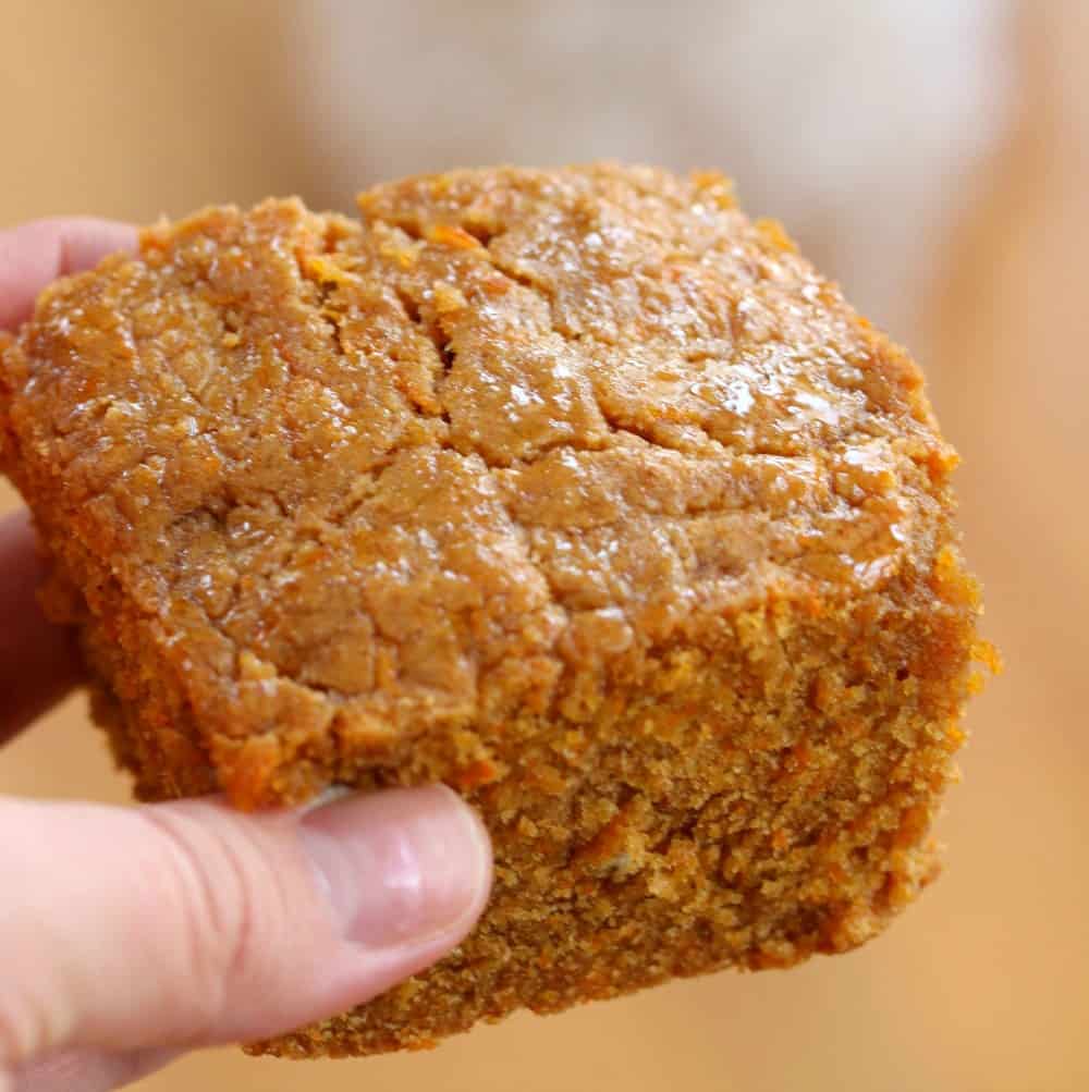 This homemade doggie cake has a tasty blend of peanut butter, honey and carrots will make this cake your furry friend's favorite treat! A hand holding up a piece of homemade dog birthday cake.