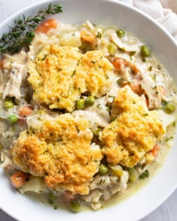 A white bowl filled with Chicken Pot Pie Casserole with fresh thyme on the side.