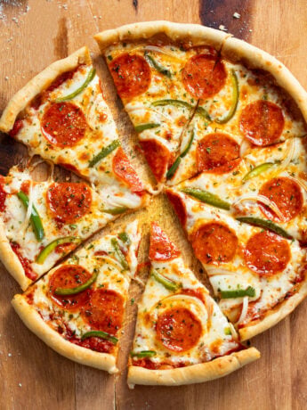 Slices of Cast Iron Skillet Pizza with pepperoni, peppers, and onions on a wooden surface.