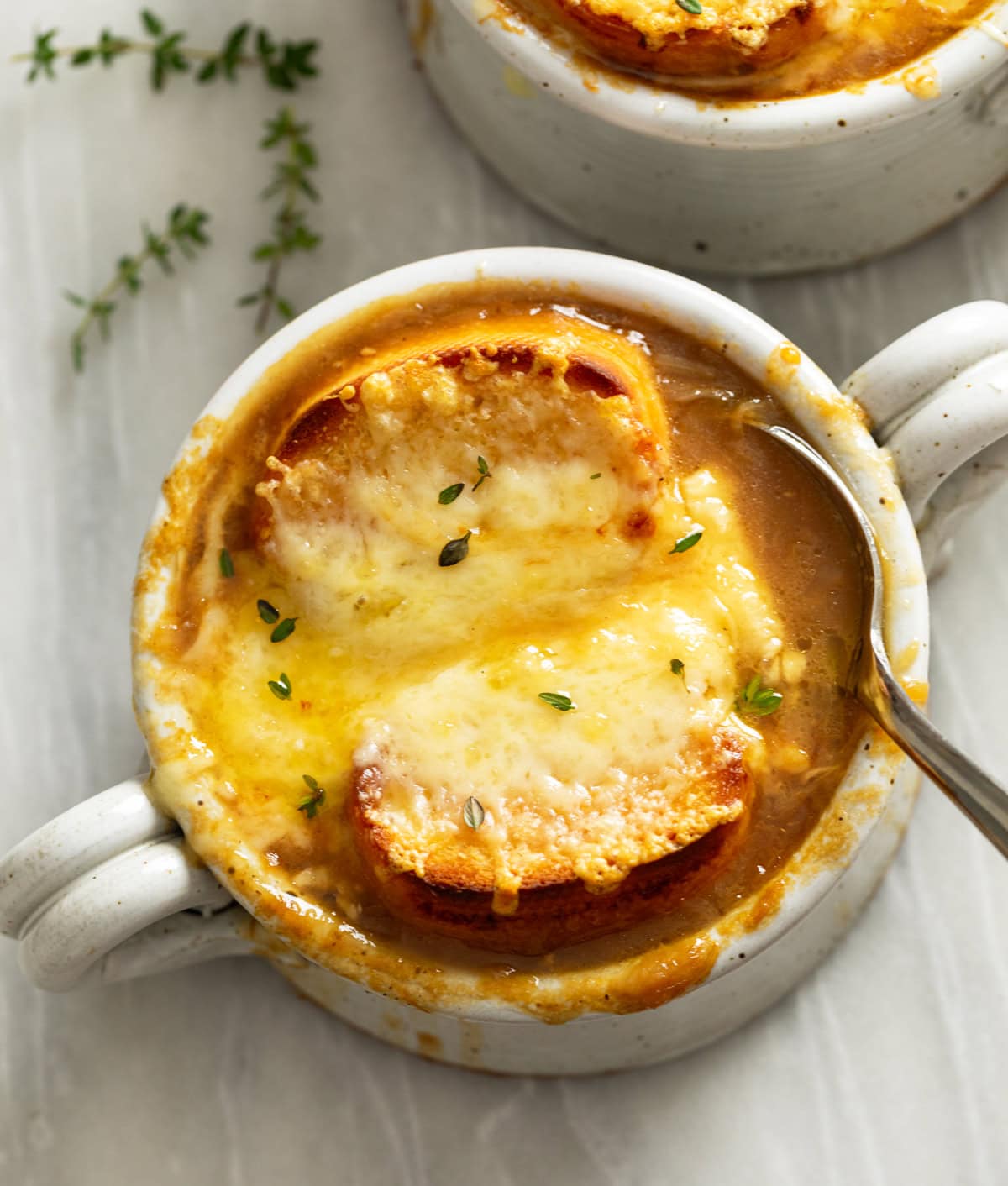 Overhead view of French Onion Soup in a crock with a spoon on the side and bread with melted cheese on top.