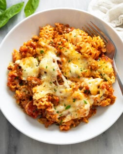 A white bowl filled with Lazy Lasagna with parsley on top and a fork on the side.