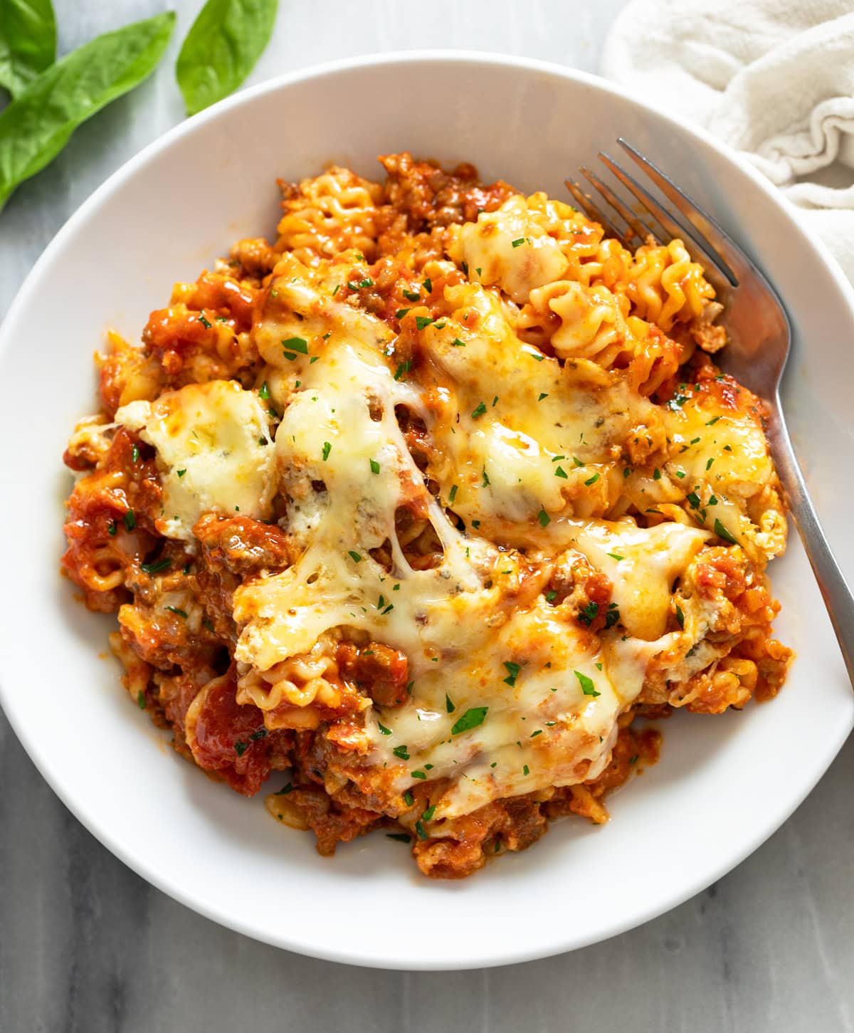 A white bowl filled with Lazy Lasagna with parsley on top and a fork on the side.